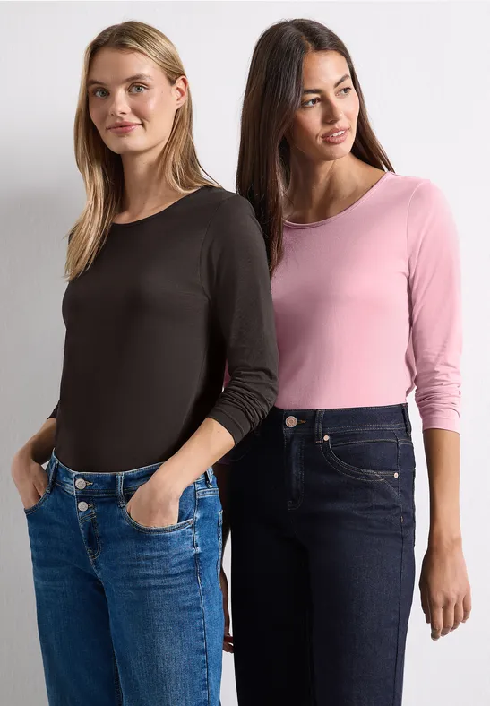 Zwei Frauen stehen nebeneinander, tragen lässige Langarmshirts und Jeans.