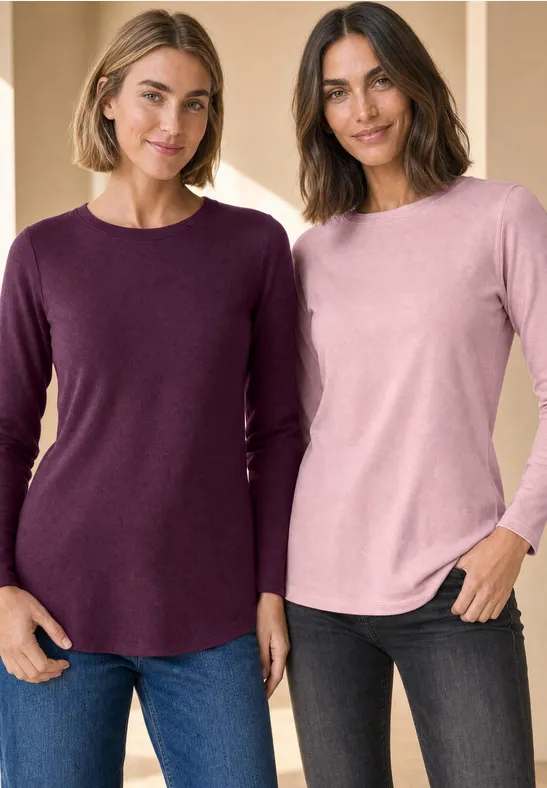 Zwei Frauen in lässigen Langarmshirts und Jeans lächeln vor hellem Hintergrund.