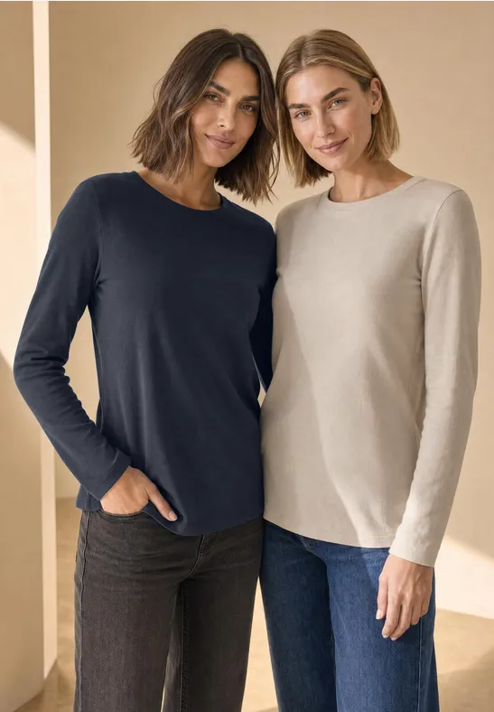 Zwei Frauen posieren Seite an Seite in lässigen Langarmshirts und Jeans.
