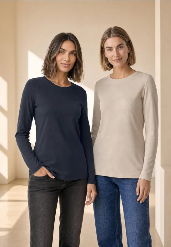 Zwei Frauen stehen in hellem Raum nebeneinander, tragen schlichte Langarmshirts und Jeans.