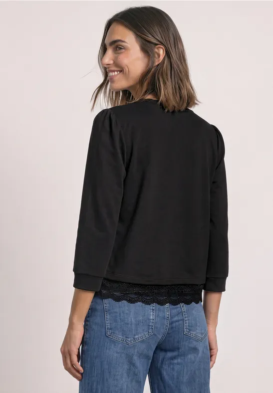 Frau in schwarzem Dreiviertel-Arm-Shirt und Jeans blickt lächelnd über die Schulter.