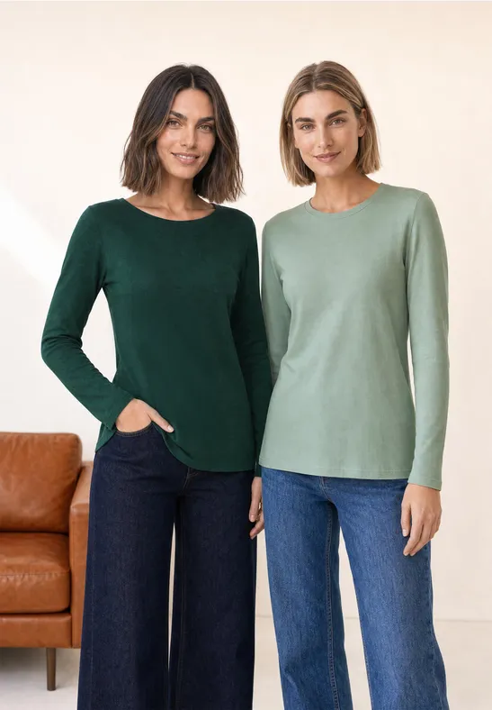Twee vrouwen in groene truien met lange mouwen en jeans poseren naast elkaar voor een lichte achtergrond.