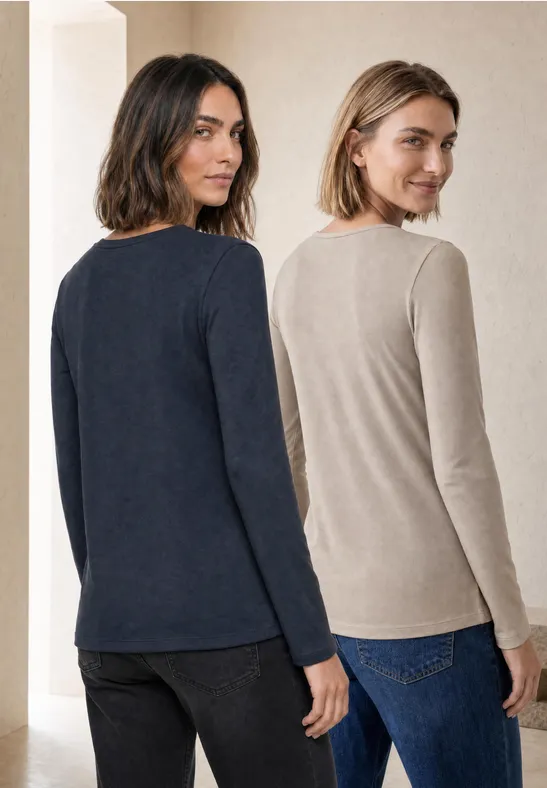 Twee vrouwen in jeans en lange mouwen (marineblauw en beige) staan naast elkaar en glimlachen.