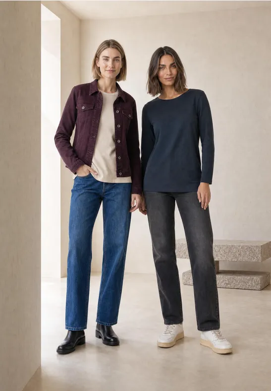 Twee vrouwen in een minimalistische setting, in jeans, truien en een jas in neutrale kleuren.