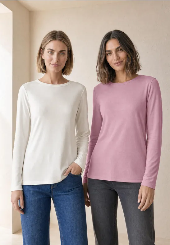 Zwei Frauen vor hellem Hintergrund tragen lässige Langarmshirts (weiß & rosa) mit Jeans und dunklen Hosen.