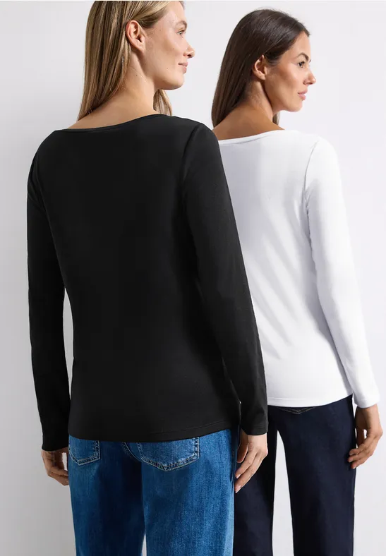 Zwei Frauen stehen Rücken an Rücken, tragen schlichte Langarmshirts in Schwarz und Weiß sowie blaue Jeans.