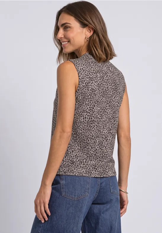 Frau von hinten in ärmellosem, gemustertem Top und Jeans, lächelnd.