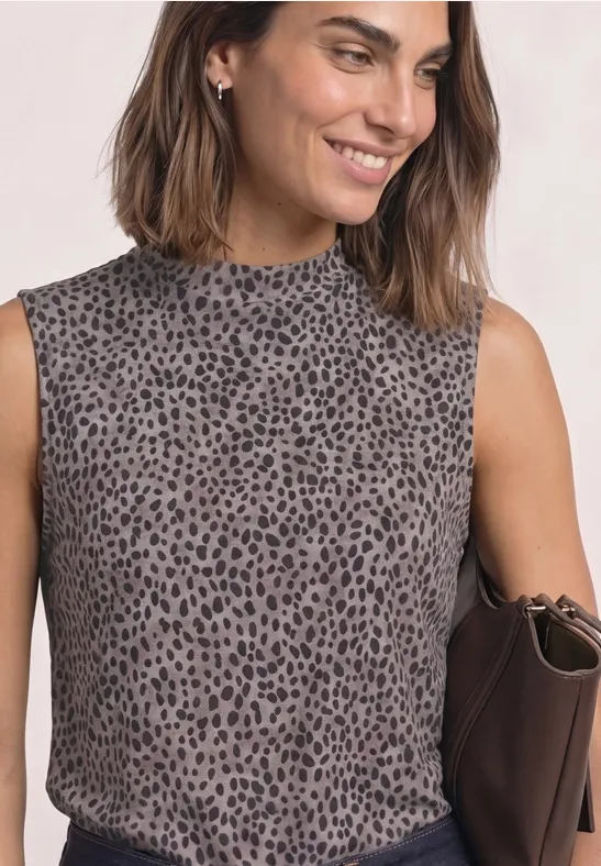 Frau trägt ärmelloses Oberteil mit dezentem Leopardenmuster, hält eine braune Clutch und lächelt.