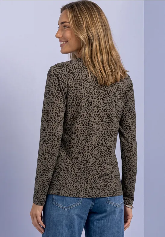 Frau in gemustertem Langarmshirt und Jeans, von hinten leicht seitlich blickend, vor hellem Hintergrund.