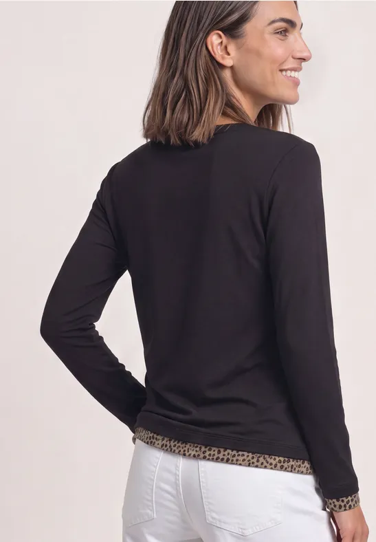 Eine Frau von hinten in schwarzem Langarmshirt mit Leo-Besatz und weißer Hose.
