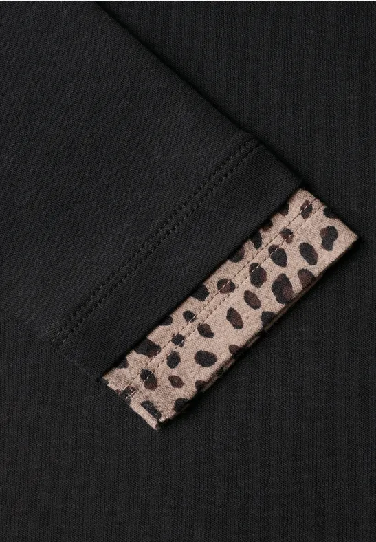 Schwarzes Kleidungsstück mit einem beige-schwarz gefleckten Leopardenprint-Bündchen am Ärmel.