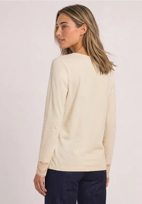 Frau in cremefarbenem Langarmshirt und dunkler Hose, Rückenansicht