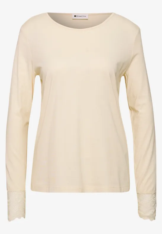Beiges Langarmshirt aus weichem Stoff mit rundem Halsausschnitt und feiner Spitzenverzierung an den Ärmeln.