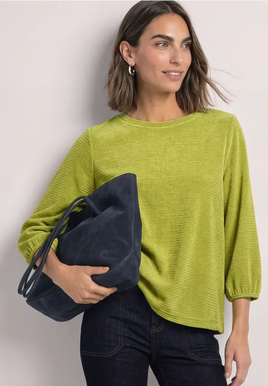 Frau in grünem Oberteil und Jeans, die eine dunkelblaue Tasche hält.
