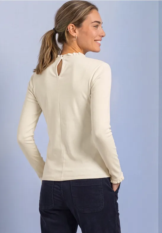 Een lachende vrouw in profiel met lichtbeige shirt, donkere jeans voor een lichte achtergrond.