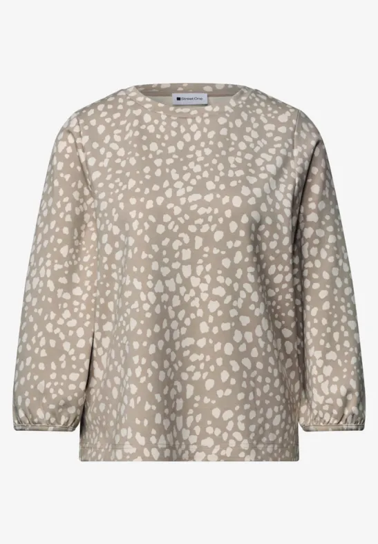 Beige Bluse mit weißem, abstraktem Tupfenmuster, locker geschnitten und mit langen Ärmeln.
