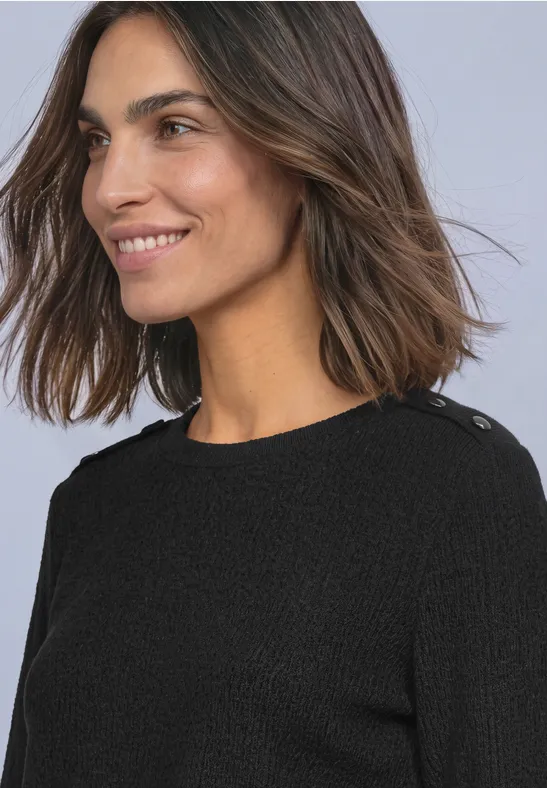 Eine lächelnde Frau mit braunen Haaren in einem schwarzen Pullover vor hellem Hintergrund.
