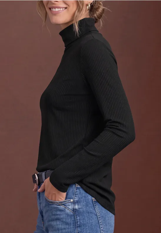 Frau im Profil in schwarzem Rollkragenpullover und blauen Jeans vor braunem Hintergrund.