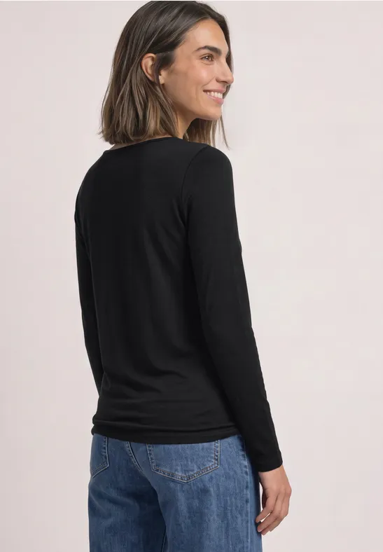 Junge Frau im Profil von hinten, trägt schwarzen Langarmshirt und Jeans, lächelt.