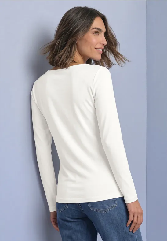 Femme en tee-shirt blanc à manches longues et jean, photographiée de dos, légèrement de côté.
