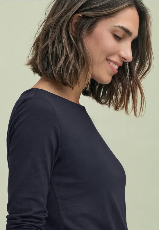 Eine lächelnde Frau in schwarzem Langarmshirt, im Profil nach unten blickend.