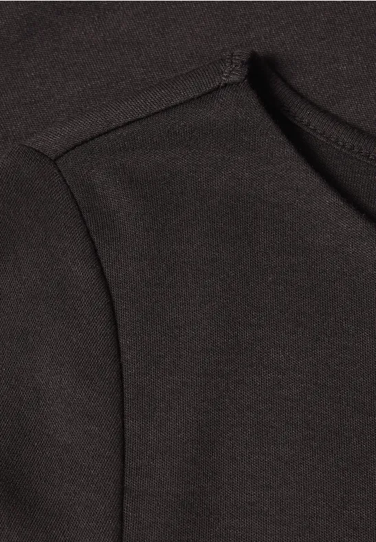 Nahaufnahme eines schwarzen Oberstoffs mit markanter Naht, vermutlich Schulterbereich eines Kleidungsstücks.