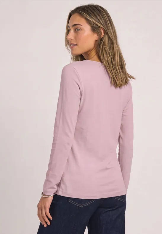 Eine Frau mit langärmligem, rosafarbenem Shirt, von hinten, Kopf leicht zur Seite gedreht.