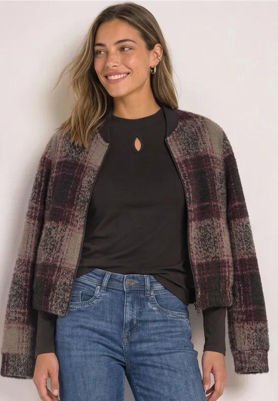 Femme souriante en veste à carreaux, haut noir et jean, posant de profil.
