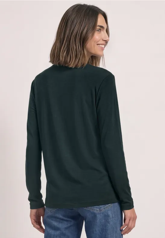 Femme de dos en top à manches longues noir et jean, se retourne en souriant.