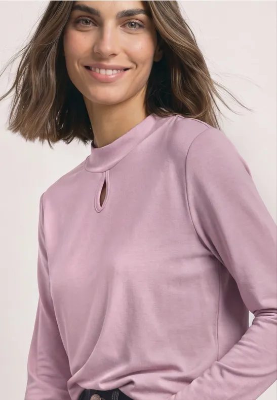 Een glimlachende vrouw in een mauve longsleeve met een kleine opening bij de hals.