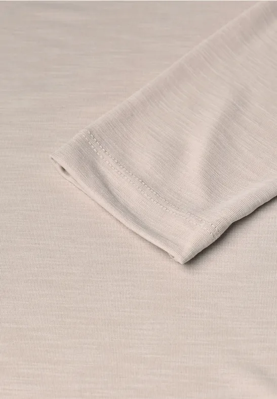 Close-up van een beige mouwuiteinde op een beige, fijn geribbeld textiel.