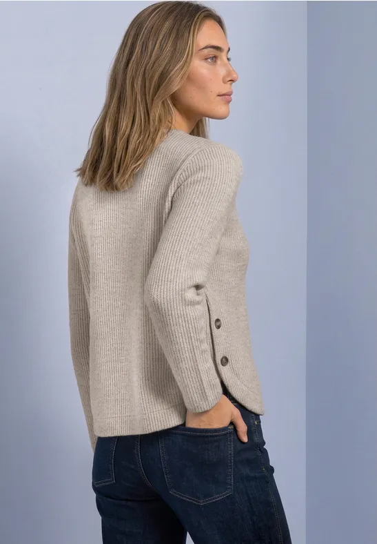 Femme de profil portant un pull beige à boutons aux manches et un jean.