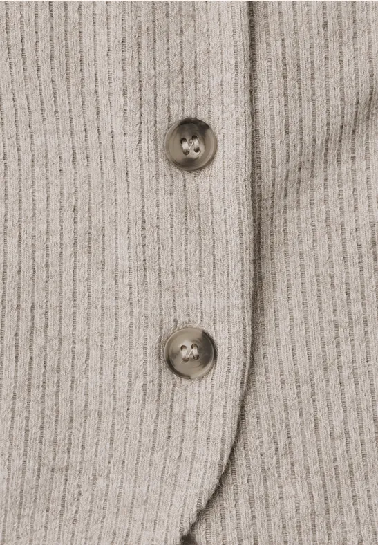 Gros plan sur un tissu en maille côtelée beige avec deux boutons bruns.