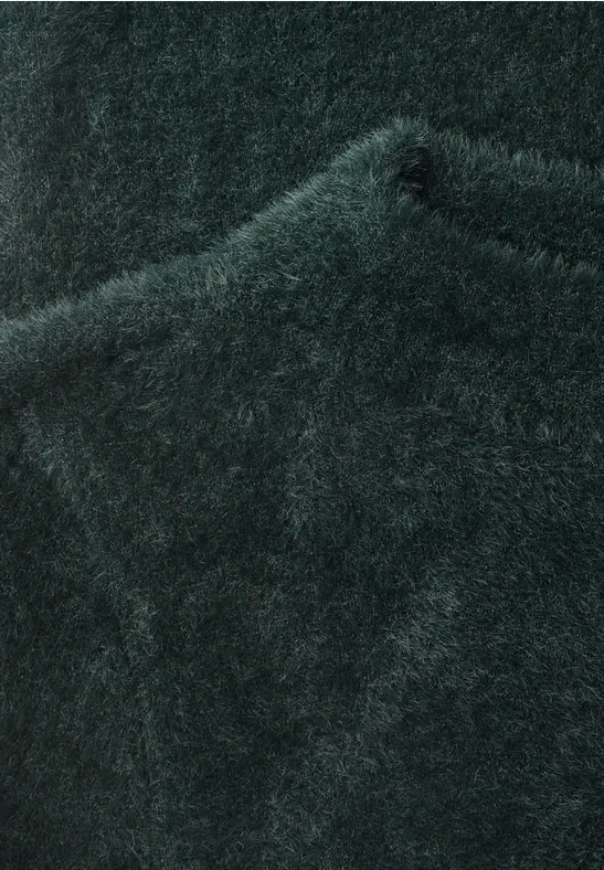 Gros plan d'un pull en maille vert foncé duveteux, au tissu moelleux et texturé.
