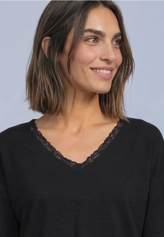 Eine lächelnde Frau mit schulterlangem braunem Haar und einem schwarzen Spitzen-V-Shirt.