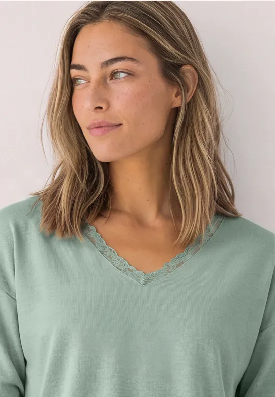Junge Frau in hellgrünem V-Ausschnitt-Shirt mit Spitzenbesatz schaut seitlich.