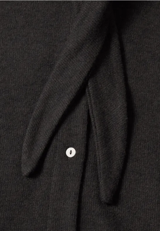 Nahaufnahme eines schwarzen Strickstücks mit zwei Bändern und einem weißen Knopf.