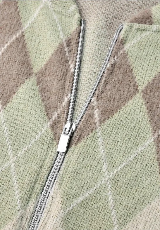 Nahaufnahme eines Strickpullovers mit Rautenmuster in Beige, Braun und Hellgrün und einem silbernen Reißverschluss.