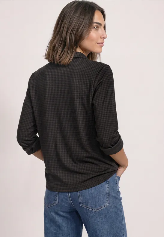 Vrouw van achteren in een donker gemêleerd shirt met lange mouwen en blauwe spijkerbroek, halflang haar.