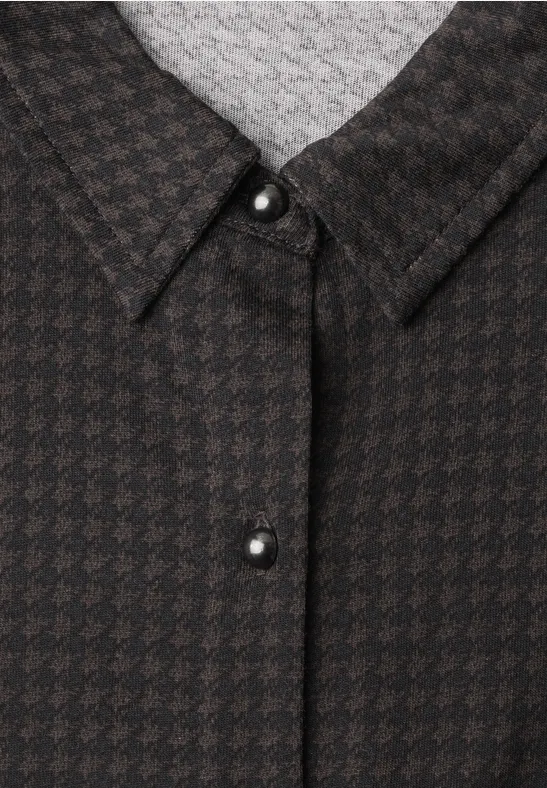 Close-up van een zwart-bruin pied-de-poule overhemdkraag met zilverkleurige knoop.