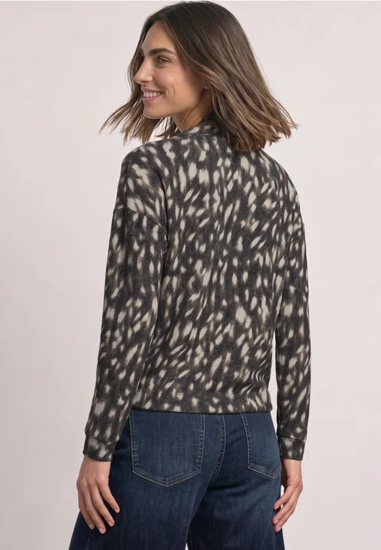 Vrouw in een zwart-beige blouse met patroon, van achteren, draait hoofd opzij en lacht.