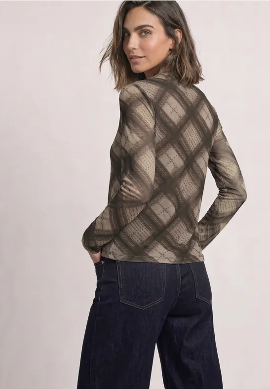 Eine Frau im braunen, karierten Rollkragenpullover und dunklen Jeans, sie blickt über die Schulter.