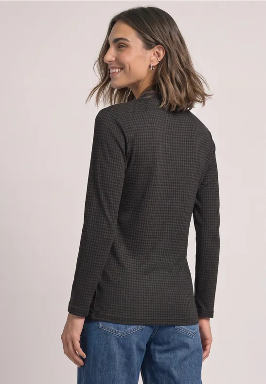 Eine Frau in Jeans und schwarzem, gestreiftem Langarmshirt blickt lächelnd über die Schulter.