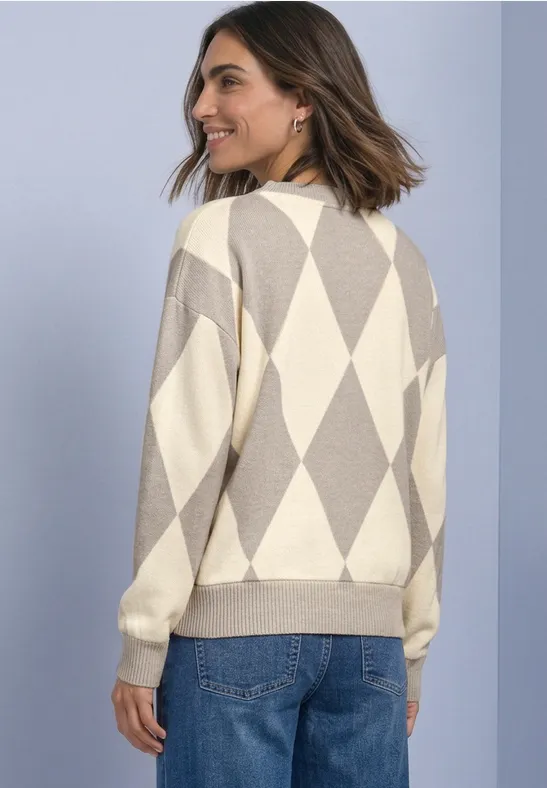 Femme de dos portant un gilet beige et crème à losanges, jean bleu et cheveux mi-longs.