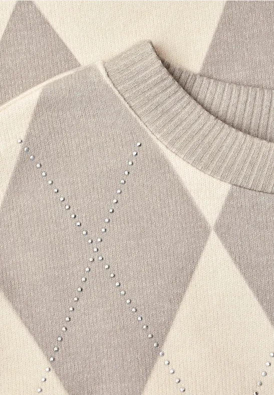 Gros plan d’un pull en maille argyle gris et beige, col côtelé et strass en forme de X.