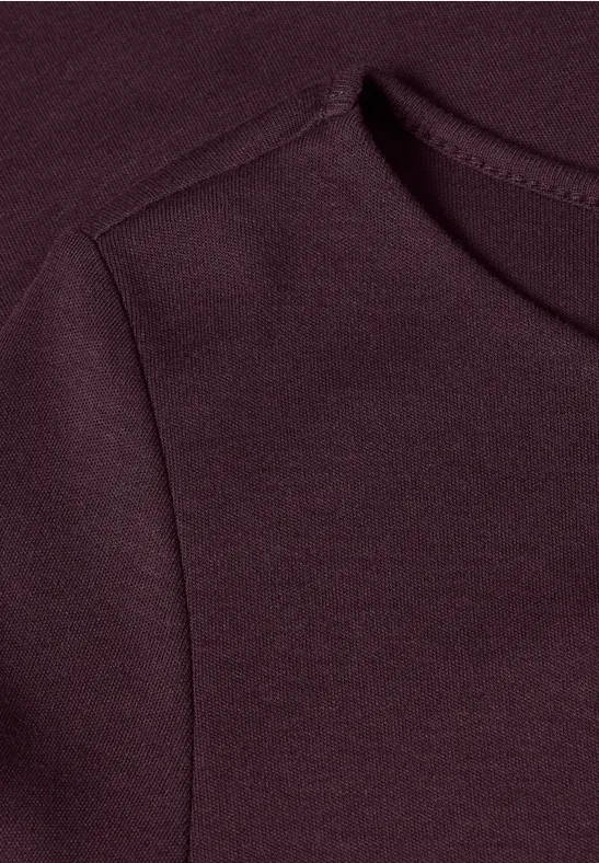 Close-up van een bordeauxkleurig kledingstuk met zichtbare schouder- en halsnaad.