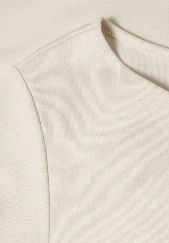 Close-up van een crèmekleurige top met ronde hals en schoudernaad.