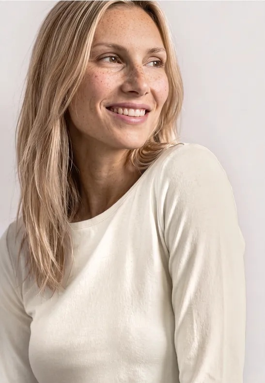 Een blonde vrouw in een wit shirt lacht opzij tegen een lichte achtergrond.