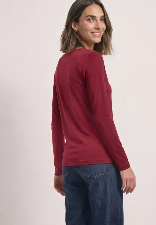Vrouw in rood shirt met lange mouwen kijkt glimlachend over haar schouder