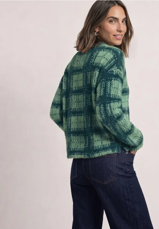Vrouw in groen-blauw geruit gebreid vest en spijkerbroek, kijkt over haar schouder.